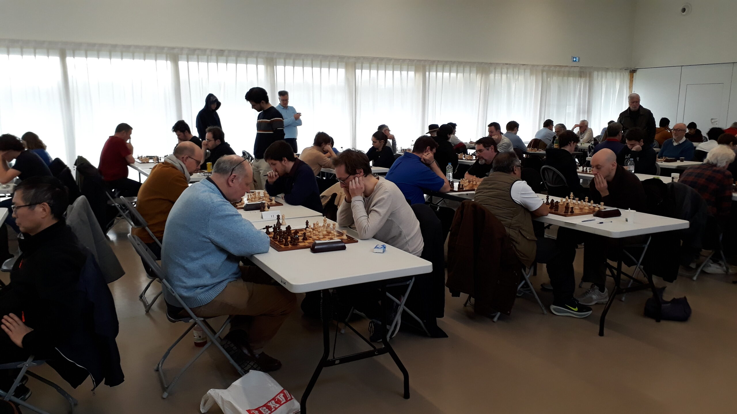Vue d’ensemble d’un tournoi d’échecs en parties lentes avec de nombreuses tables et joueurs.