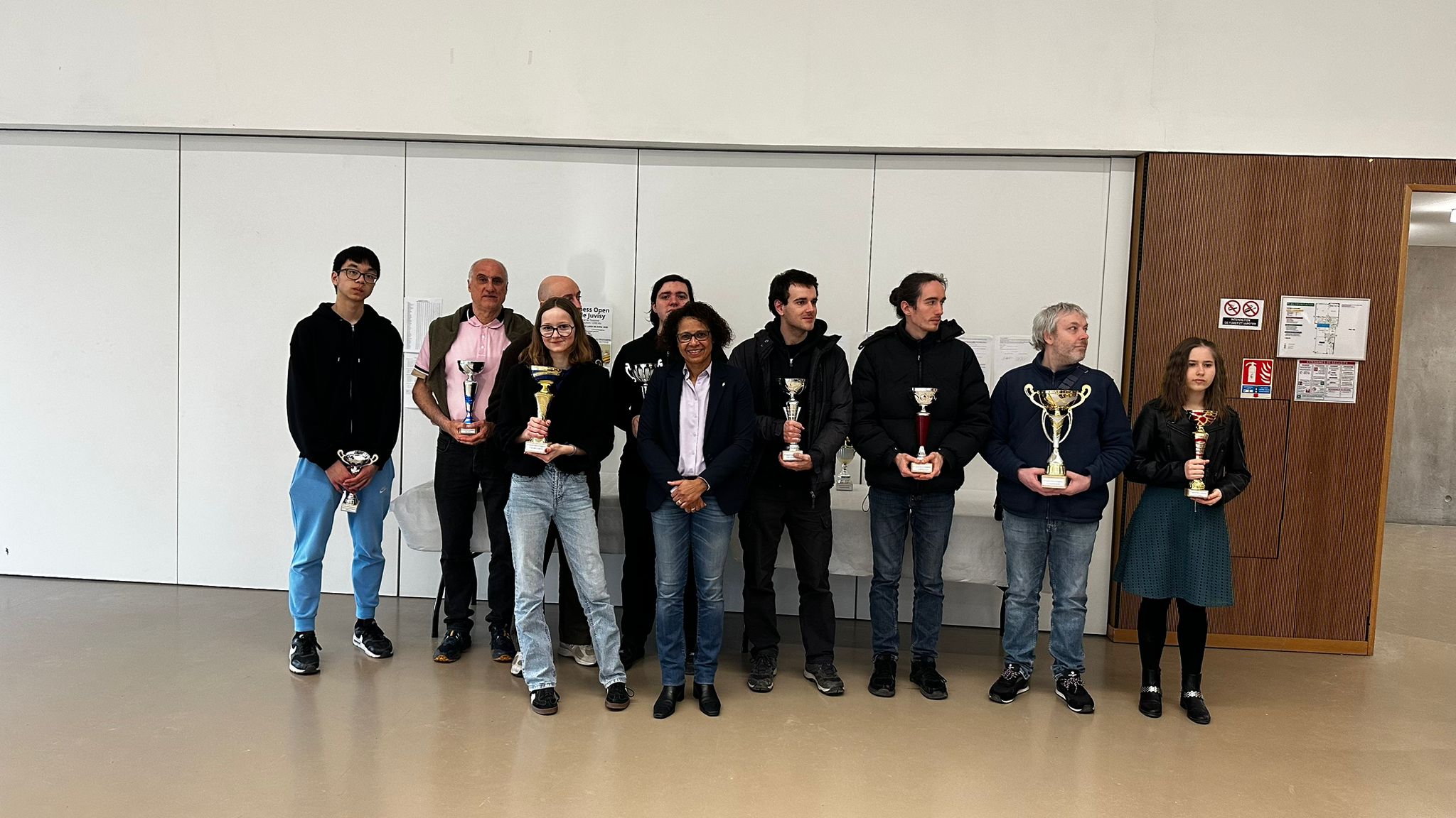 Remise des prix d’un tournoi d’échecs : plusieurs lauréats et organisateurs posent avec des coupes.