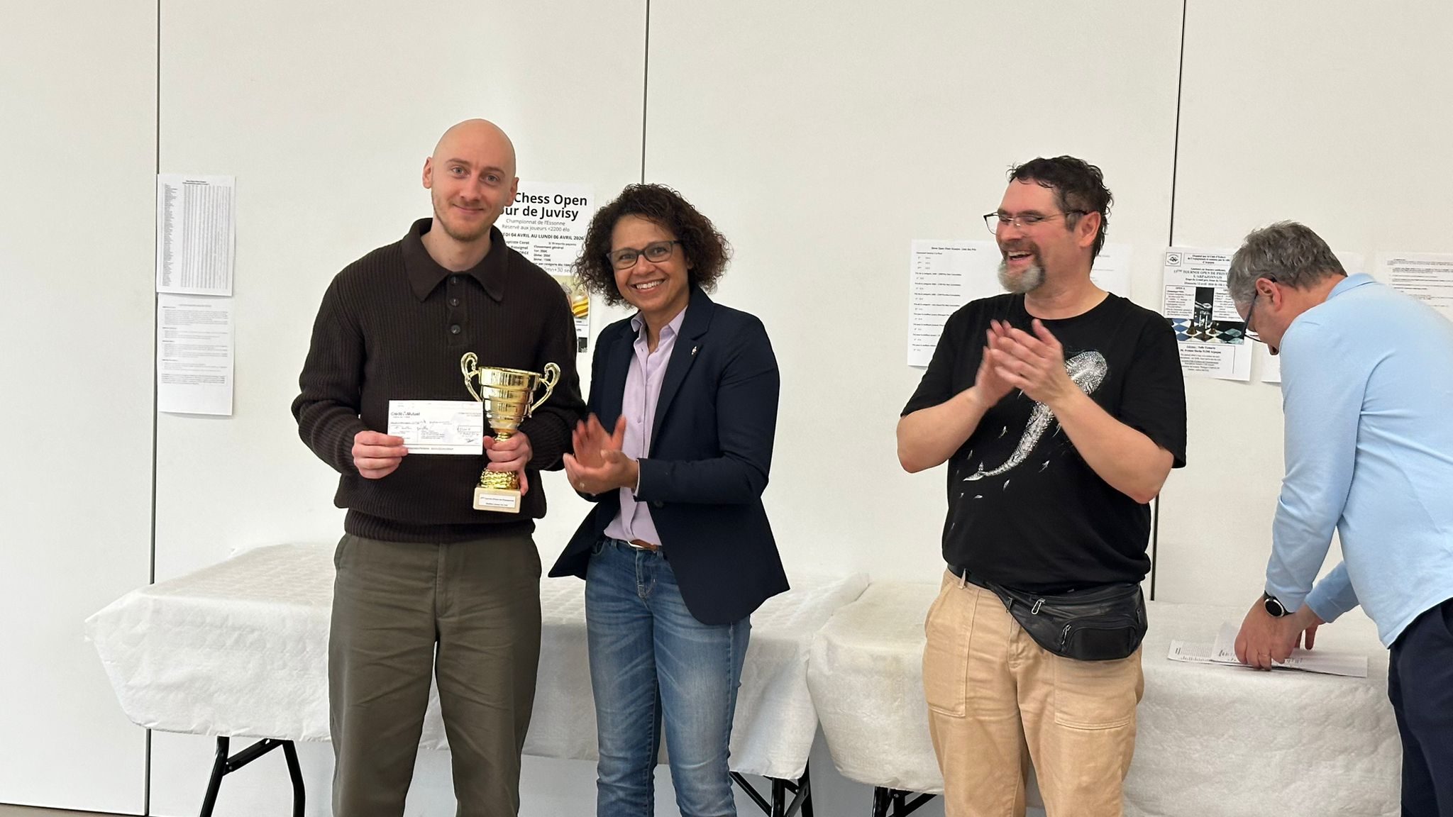 Un lauréat reçoit une coupe et un chèque pendant la remise des prix d’un open d’échecs.