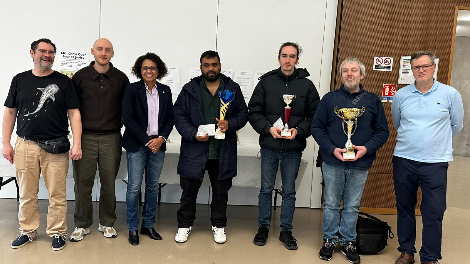 Trois lauréats posent avec leurs trophées pendant la remise des prix d’un open d’échecs.